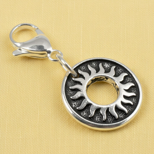 Hackberry Creek silver-plated pewter sun charm with a stainless steel lobster clasp on a textured yellow background.