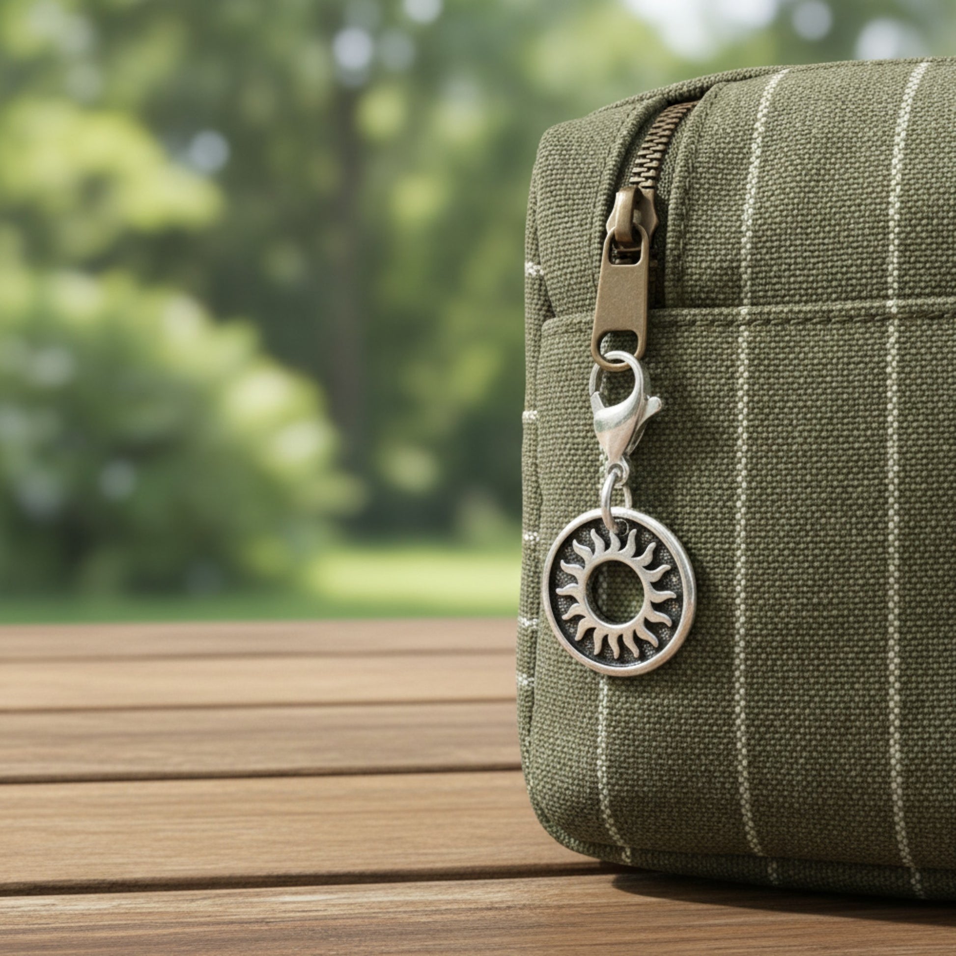 Hackberry Creek silver sun charm with lobster clasp attached to a green striped canvas bag on a wooden table.