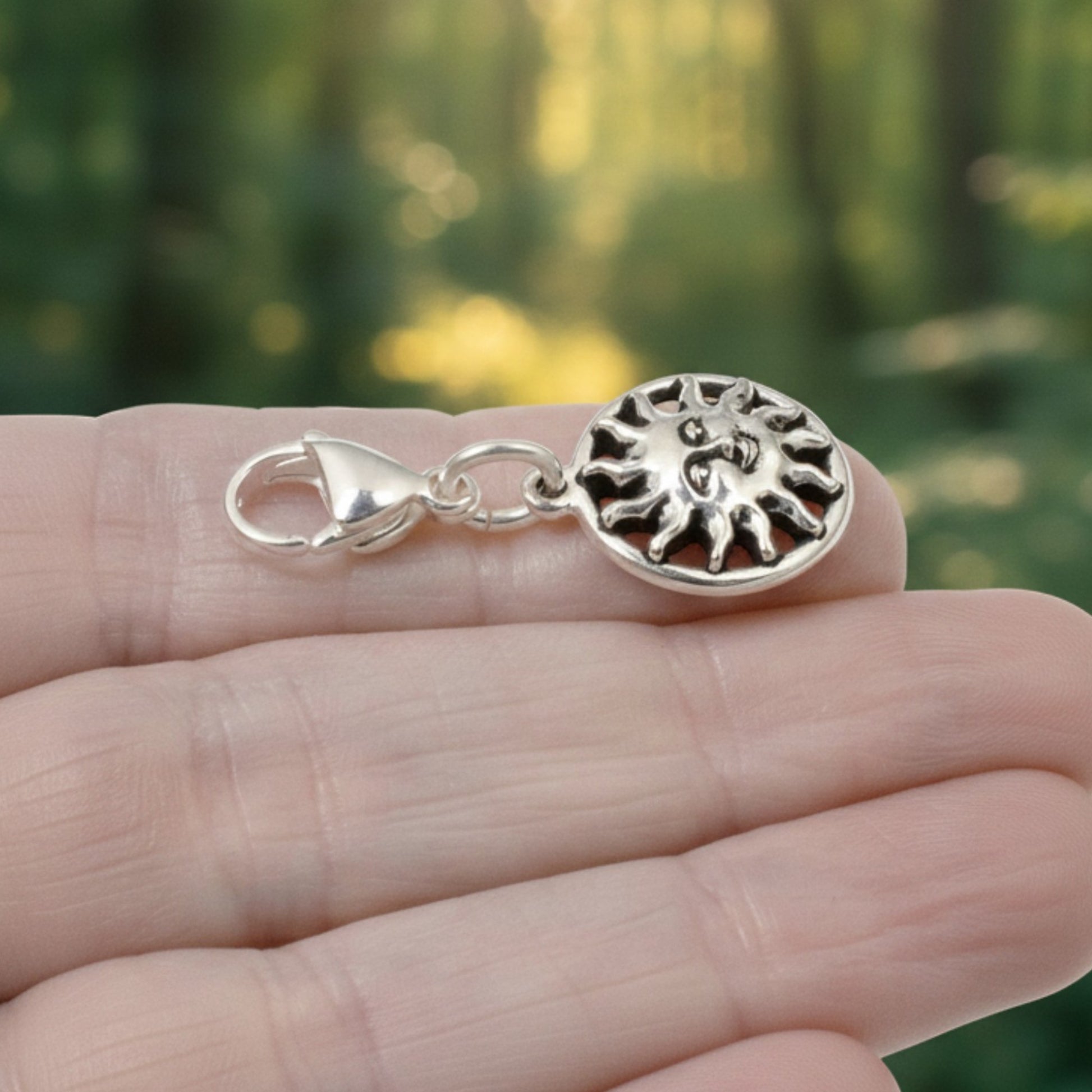 Hackberry Creek silver sun charm with a lobster clasp held in a hand against a blurred forest background.