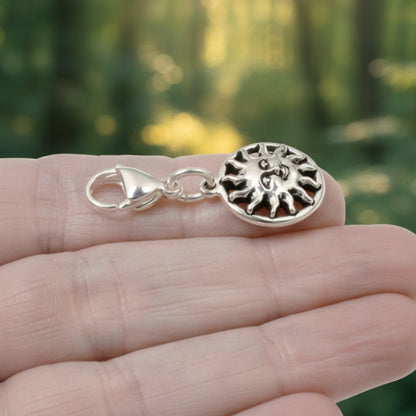 Hackberry Creek silver sun charm with a lobster clasp held in a hand against a blurred forest background.
