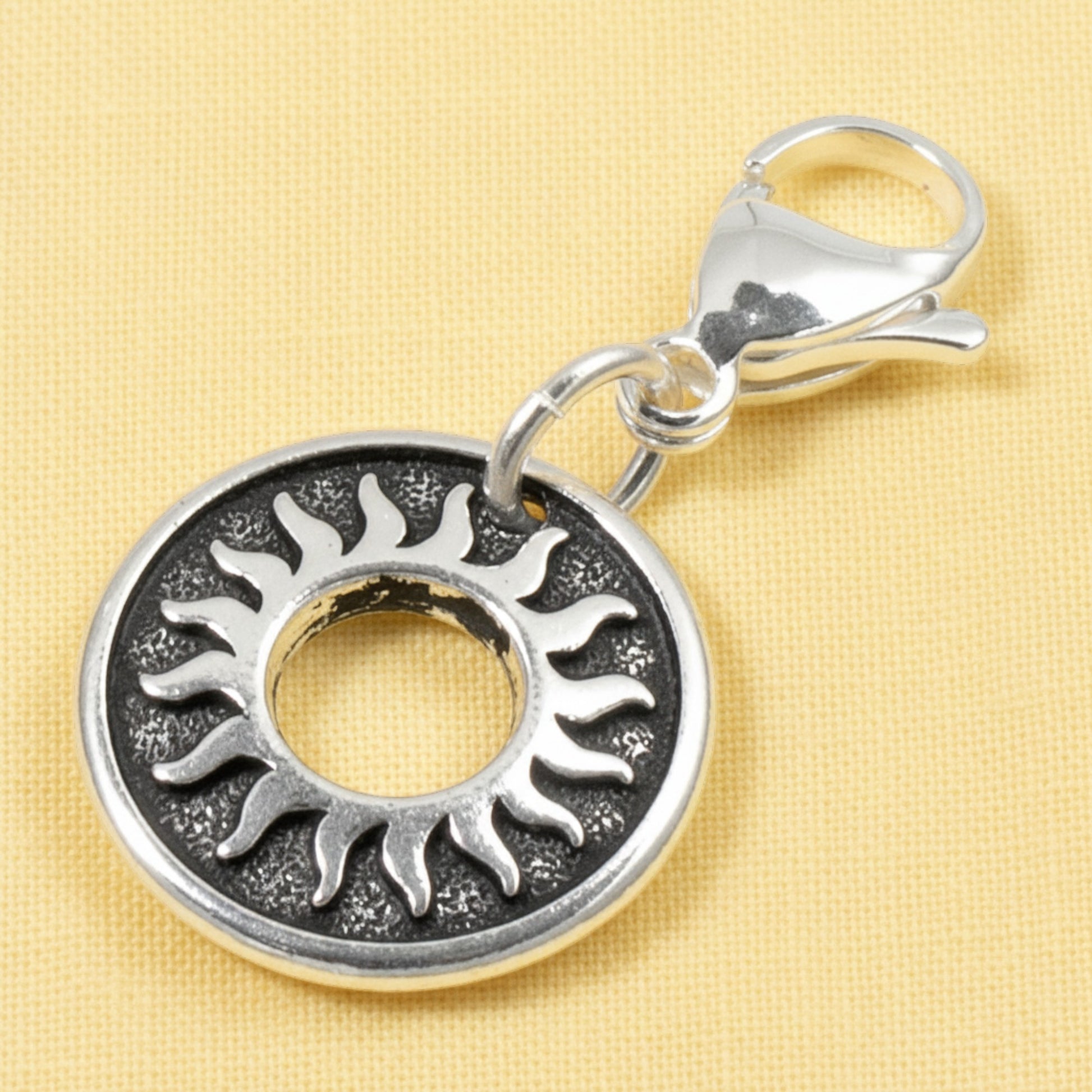 Hackberry Creek silver celestial sun charm with a stainless steel lobster clasp on a yellow background.