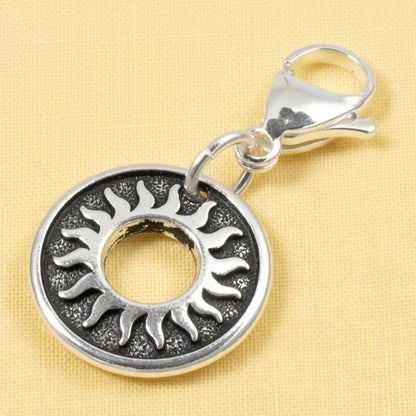 Hackberry Creek silver celestial sun charm with a stainless steel lobster clasp on a yellow background.