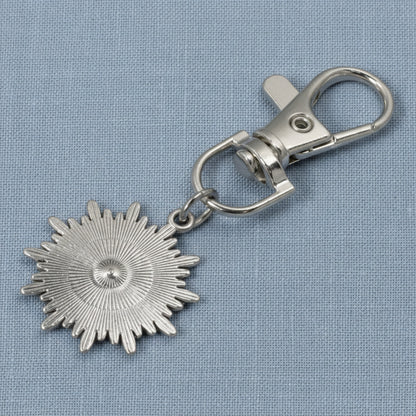 Hackberry Creek silver metal alloy sunburst evil eye key fob charm with a clear rhinestone accent on a blue background