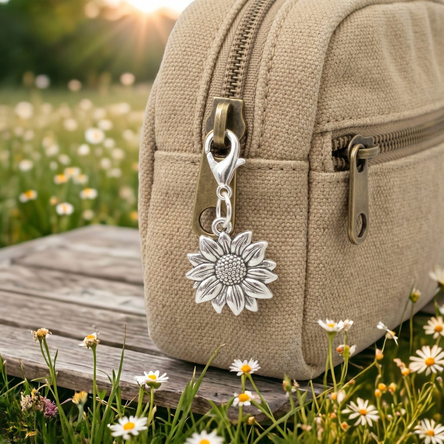 Hackberry Creek silver-plated sunflower charm clipped to a beige canvas bag in a sunny field of daisies.