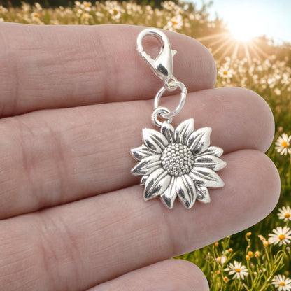 Hackberry Creek silver sunflower clip-on charm held in hand against a blurred field of daisies.
