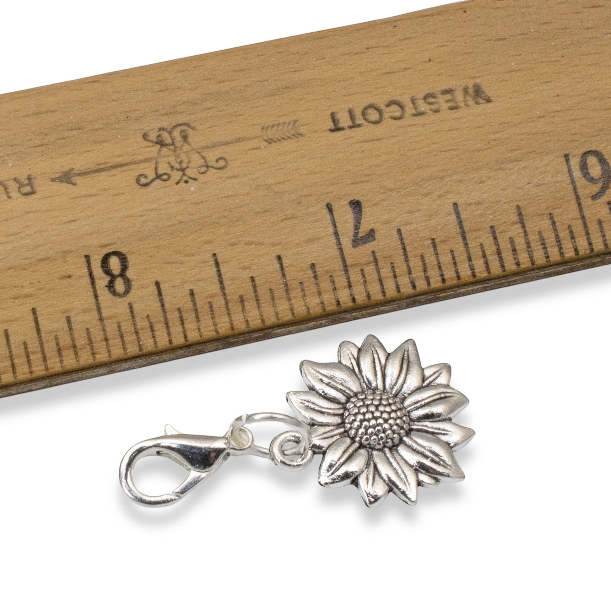Hackberry Creek silver sunflower clip-on charm next to a wooden ruler for scale, showing floral metal detail.