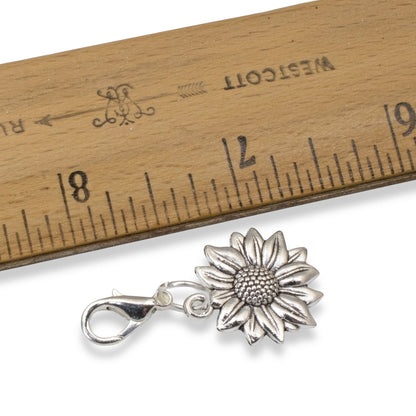 Hackberry Creek silver sunflower clip-on charm next to a wooden ruler for scale, showing floral metal detail.