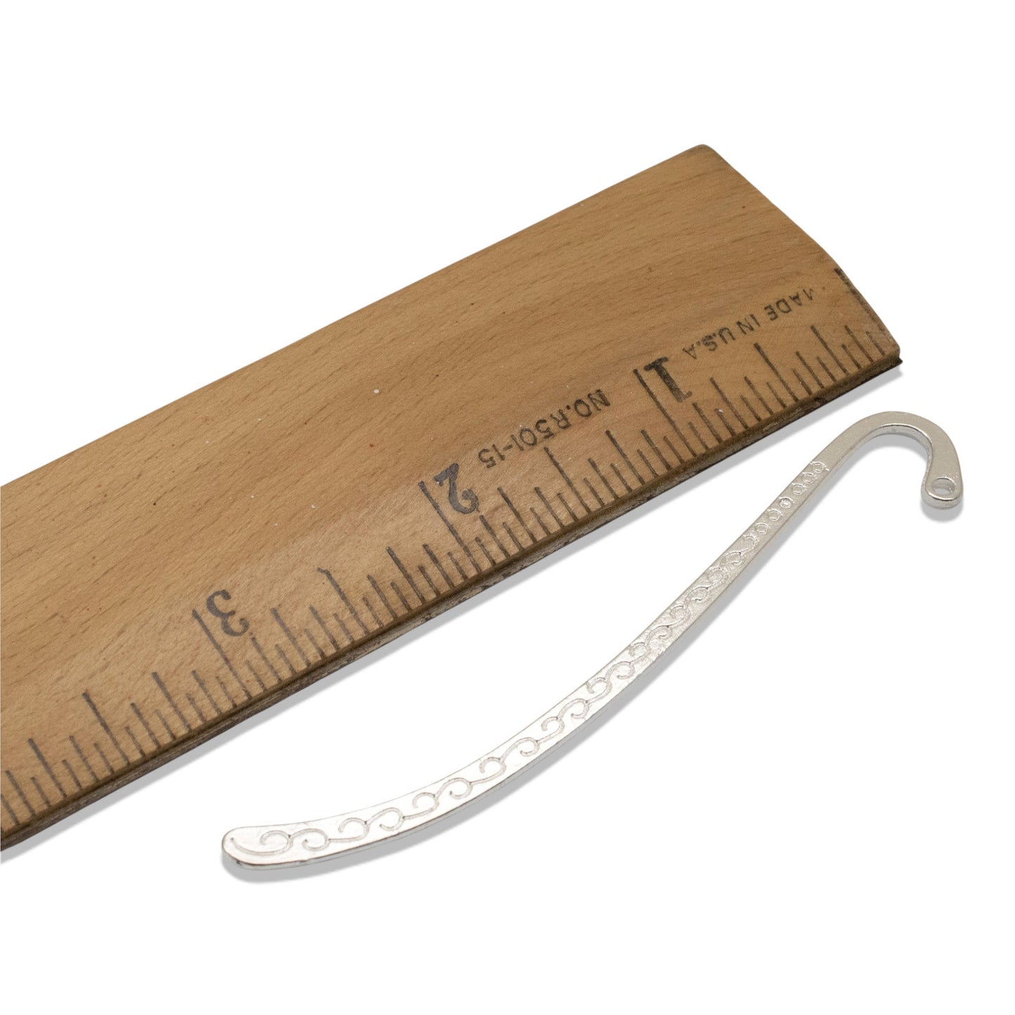 Hackberry Creek silver-tone zinc alloy hook bookmark blank with Tibetan swirl detail next to a wooden ruler.