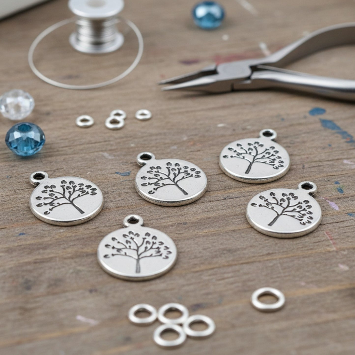 Hackberry Creek antique silver tree of life coin charms for jewelry making on a wooden craft table with tools