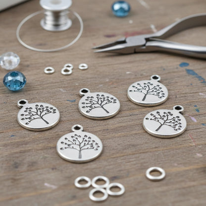 Hackberry Creek antique silver tree of life coin charms for jewelry making on a wooden craft table with tools