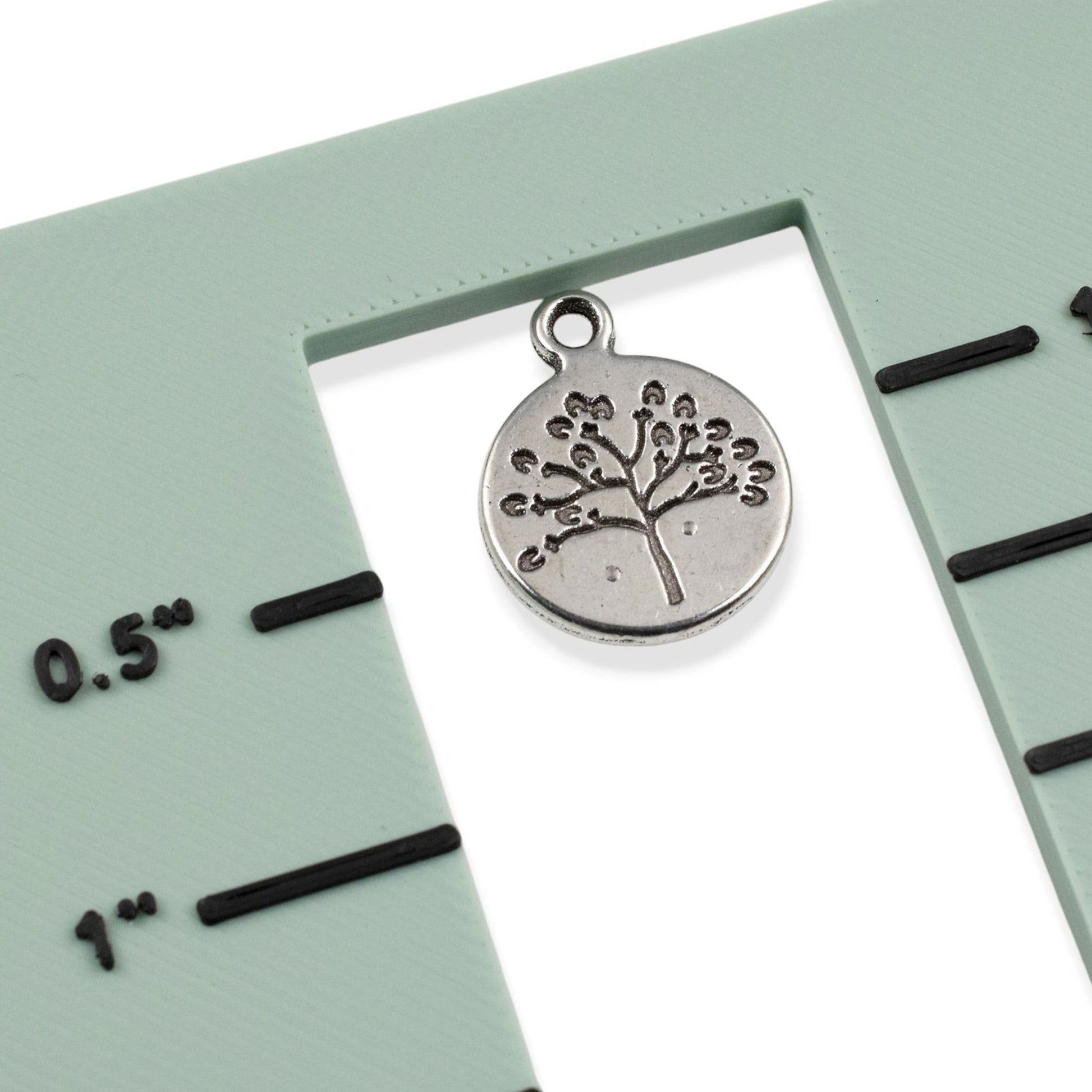 Hackberry Creek antique silver tree of life coin charm on a green measuring tool for jewelry making scale reference