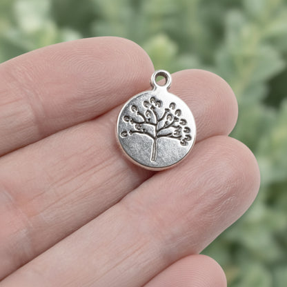 Hackberry Creek antique silver tree of life coin charm held between fingers for scale