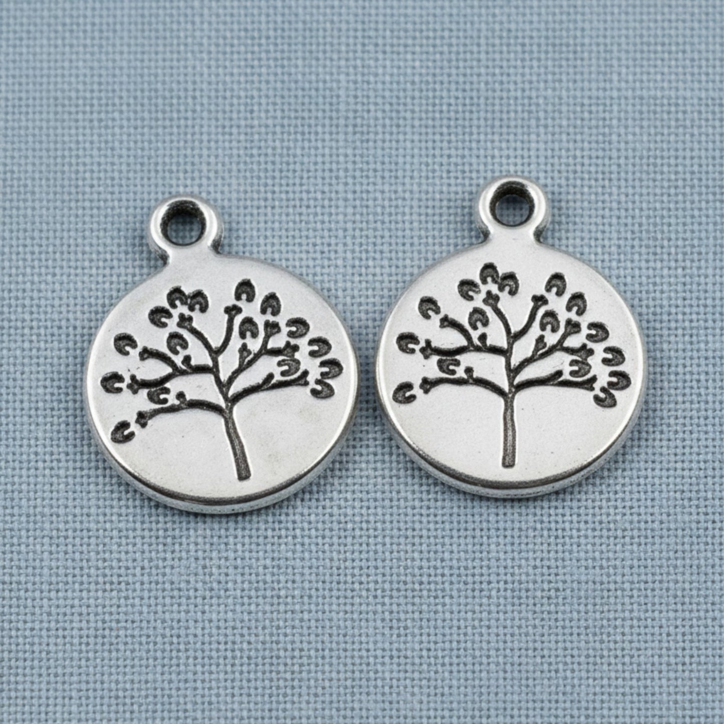 Hackberry Creek antique silver tree of life coin charms for spiritual jewelry making on a blue fabric background