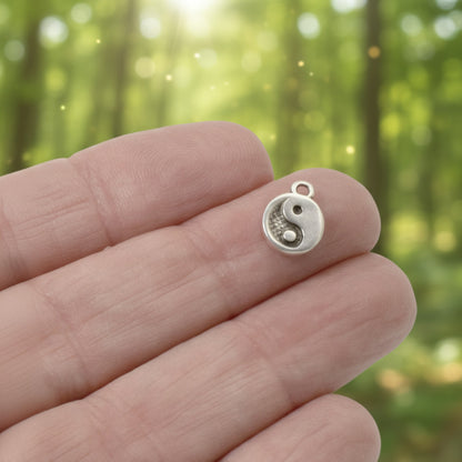 Hackberry Creek mini silver yin yang charm held on a finger against a blurred forest background