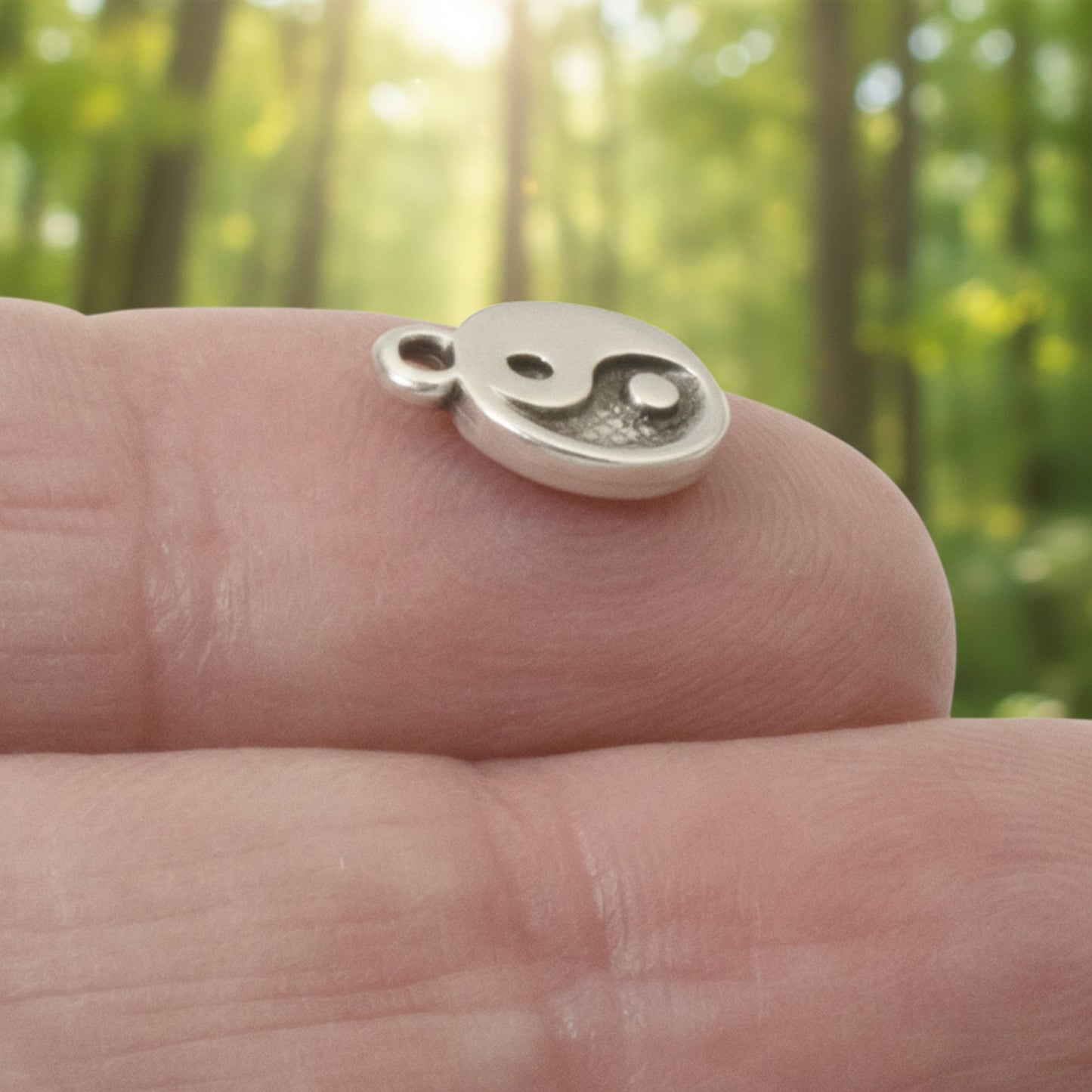 Hackberry Creek mini silver yin yang charm held on a fingertip, featuring an antique finish for jewelry making.