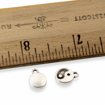 Hackberry Creek mini silver yin yang charms with antique finish shown next to a ruler for scale.