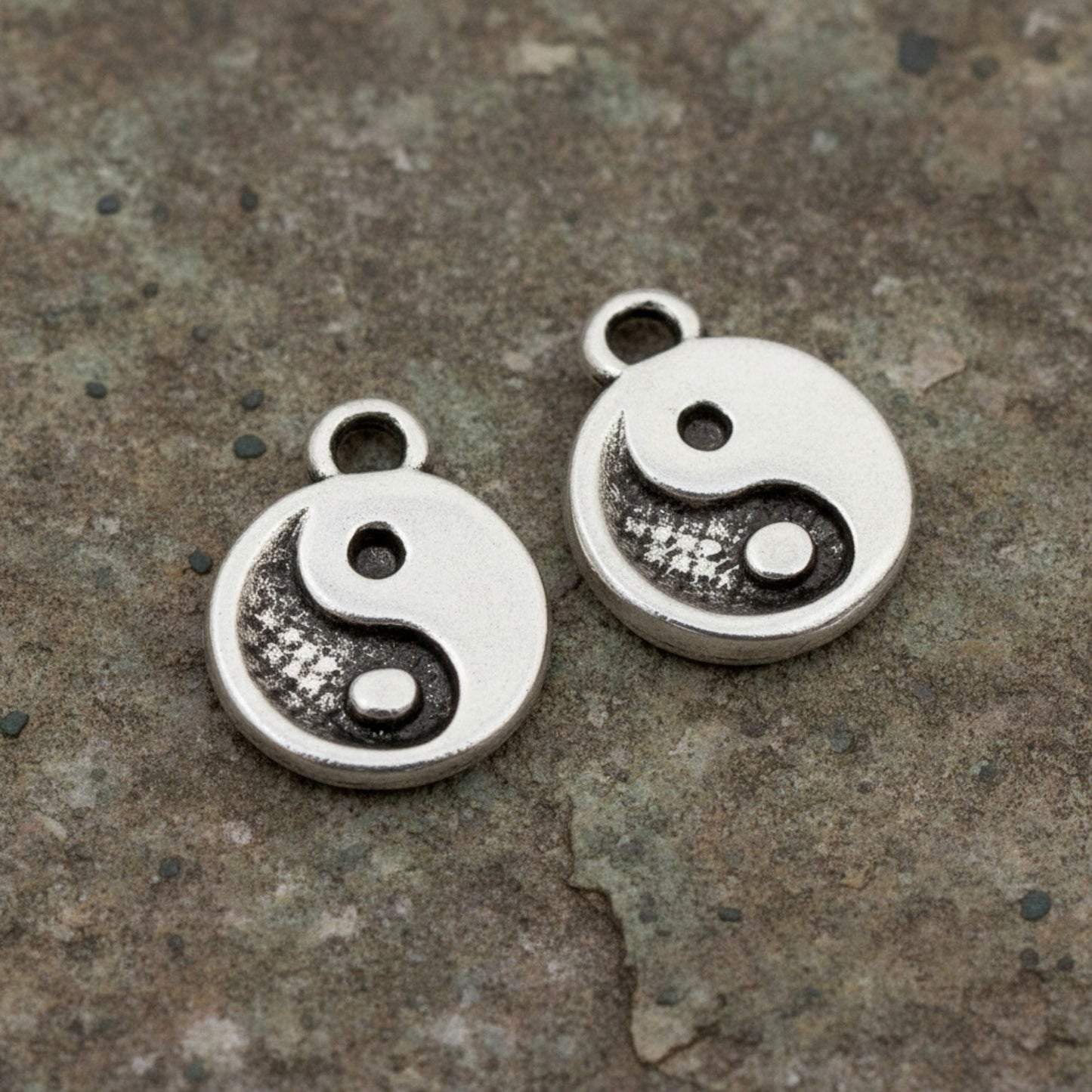 Hackberry Creek mini silver yin yang charms with antique finish on a textured stone background