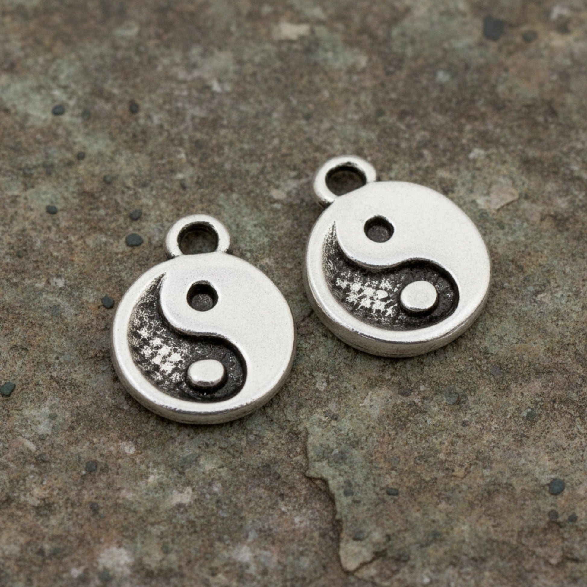 Hackberry Creek mini silver yin yang charms with antique finish on a textured stone background