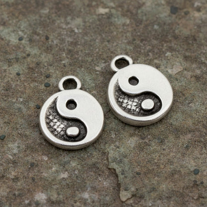 Hackberry Creek mini silver yin yang charms with antique finish on a textured stone background