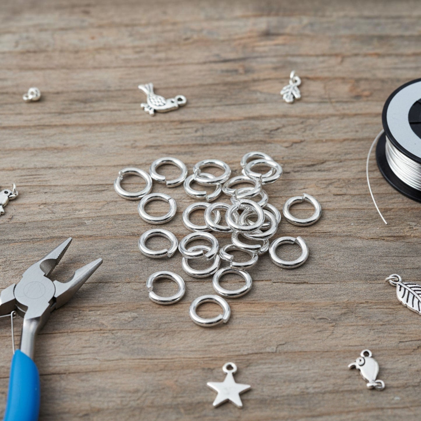 Hackberry Creek 8mm bright silver 304 stainless steel jump rings on a wooden surface with jewelry pliers and charms.