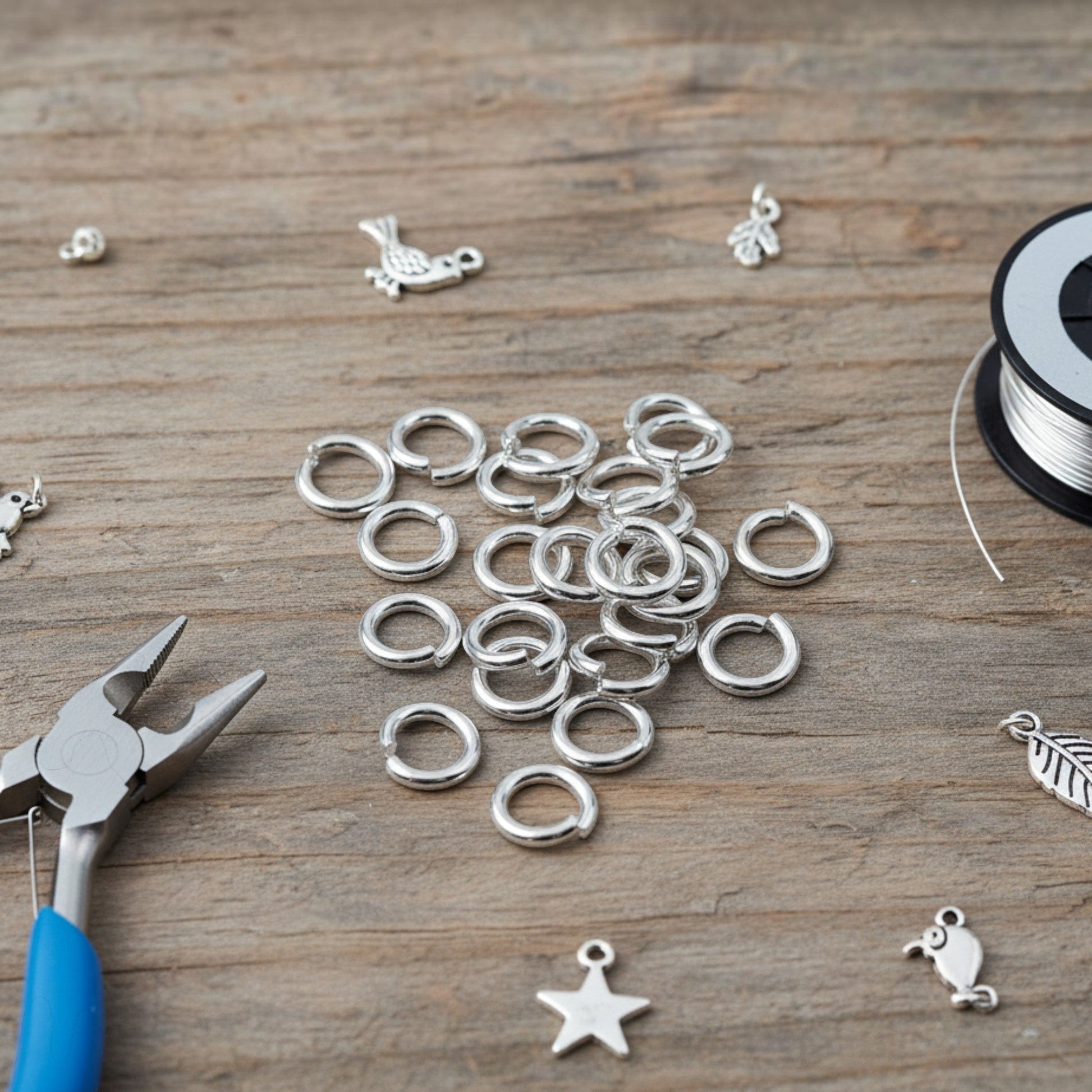 Hackberry Creek 8mm bright silver 304 stainless steel jump rings on a wooden surface with jewelry pliers and charms.