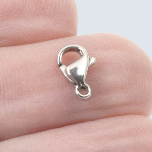 Hackberry Creek 6x9mm dark silver stainless steel lobster claw clasp held on a finger for scale