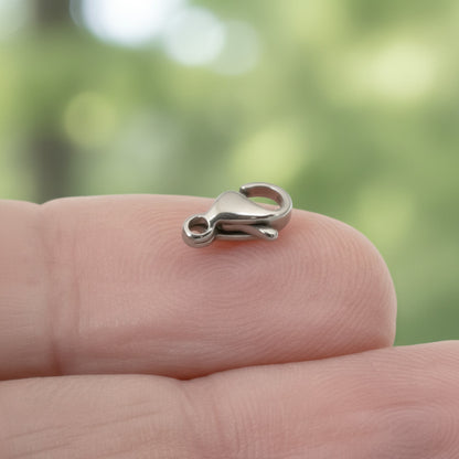 Hackberry Creek tiny 6x9mm dark silver stainless steel lobster claw clasp held on a fingertip for scale.