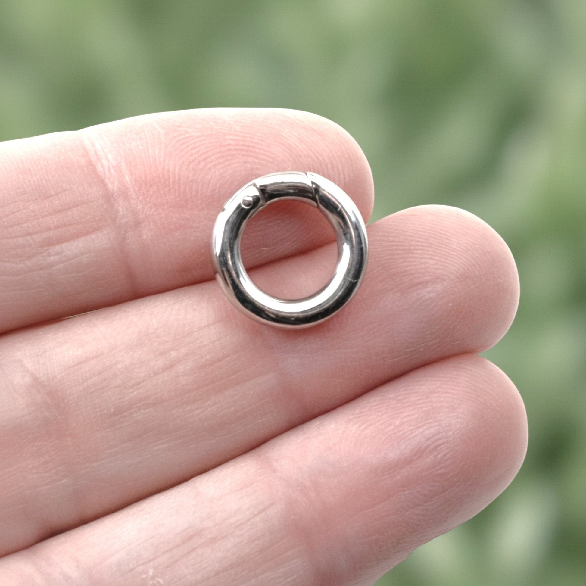 Hackberry Creek 15mm round stainless steel carabiner spring clasp in polished silver held between fingers.