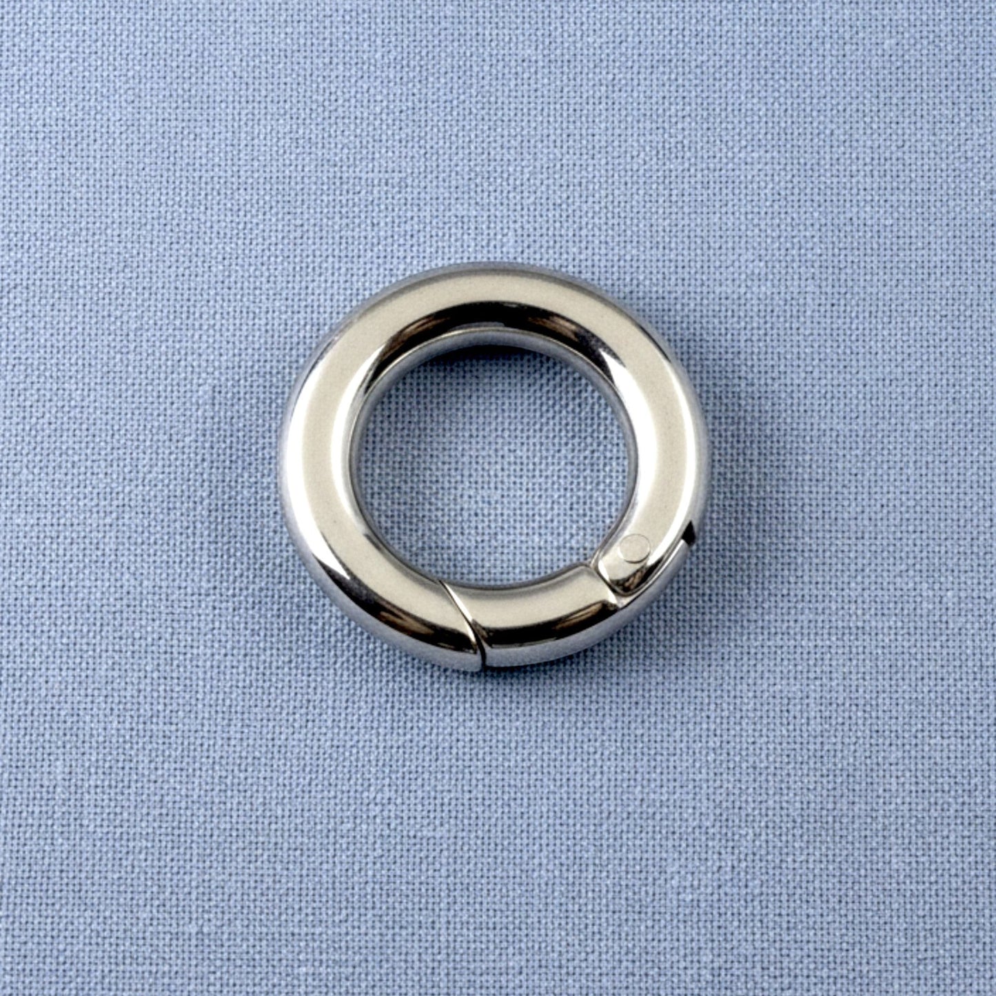 Hackberry Creek 15mm round stainless steel carabiner spring clasp with a polished silver finish on a blue fabric background