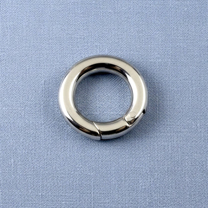 Hackberry Creek 15mm round stainless steel carabiner spring clasp with a polished silver finish on a blue fabric background