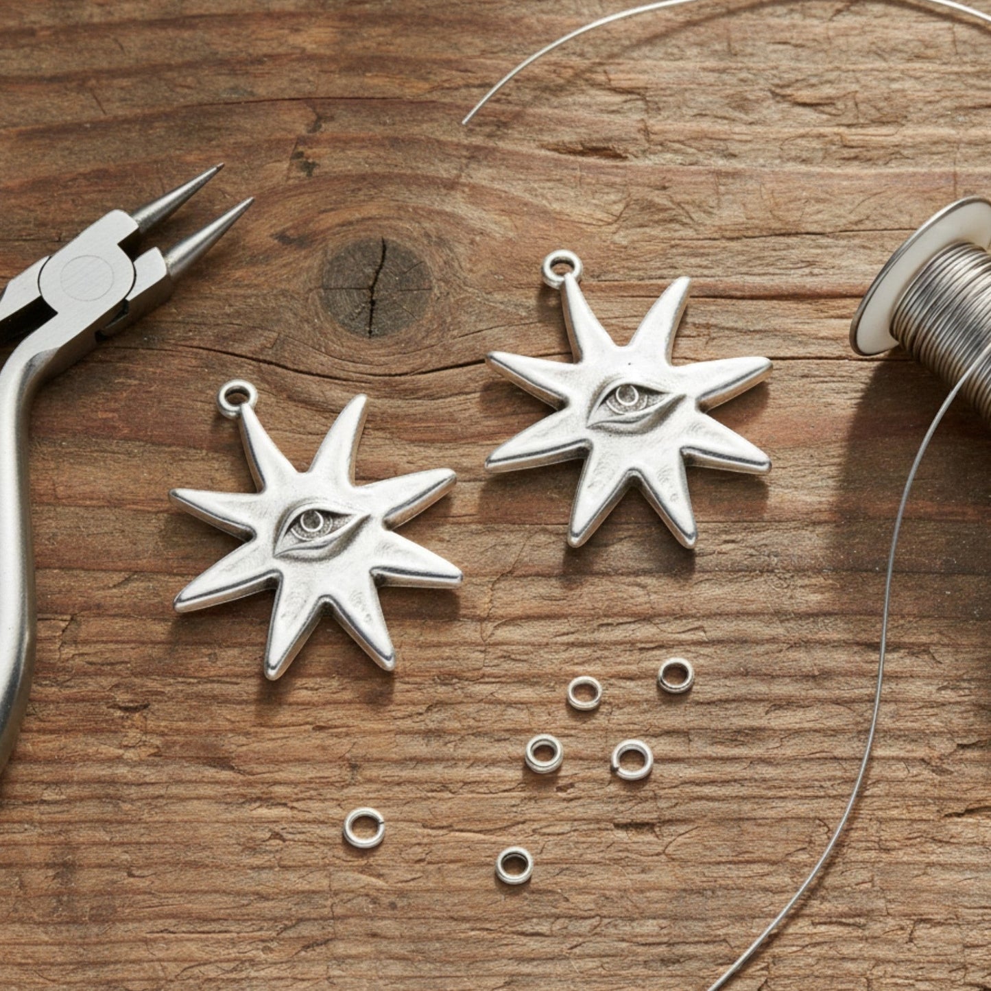 Hackberry Creek silver star eye pendants with jewelry pliers and wire on a rustic wooden table.
