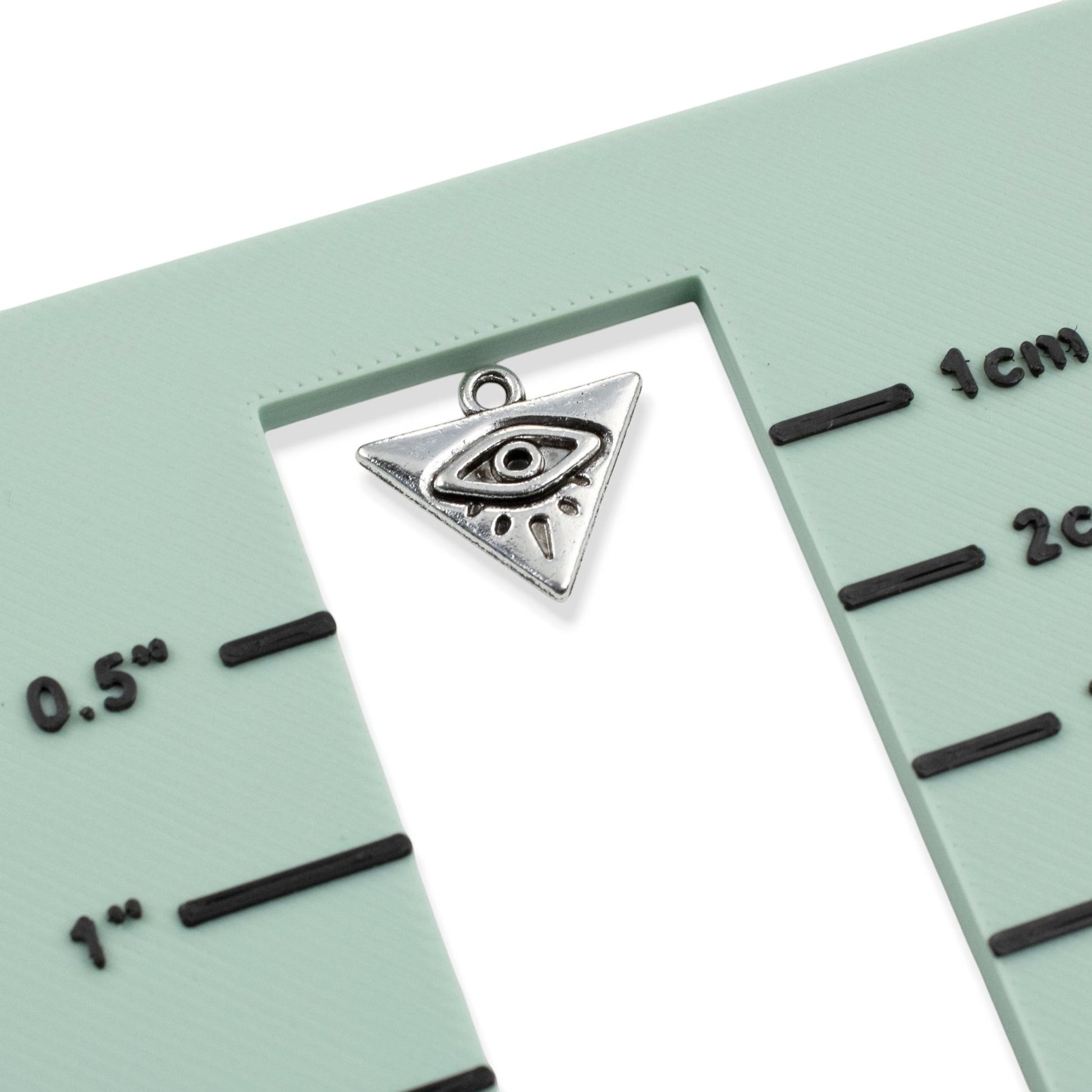 Hackberry Creek antique silver triangle evil eye charm on a green measurement tool for jewelry making scale reference