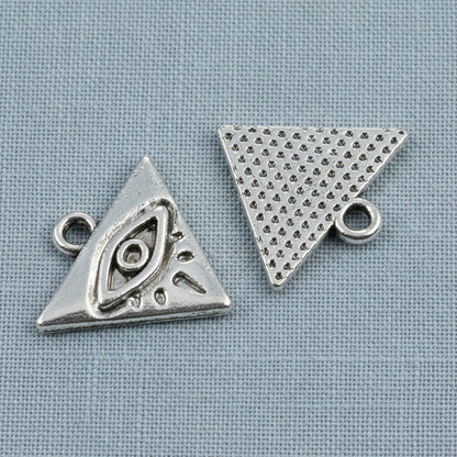 Hackberry Creek antique silver triangle evil eye charms for mystical jewelry making on a blue fabric background
