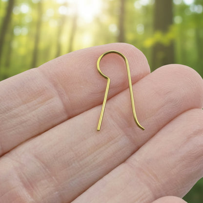 Hackberry Creek yellow niobium earring hook held in a hand against a blurred forest background